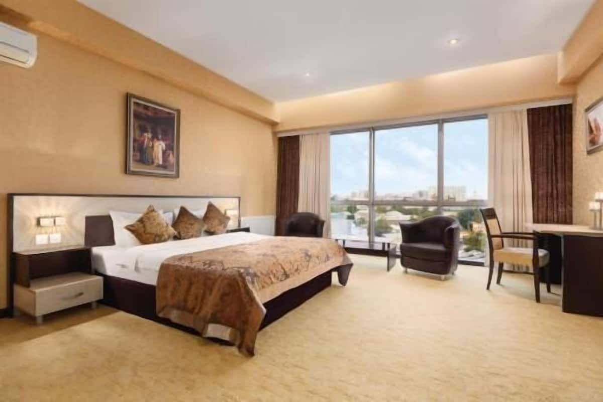 Ein Hotelzimmer mit einem großen Bett, einem Schreibtisch, einem Stuhl und Blick auf die Stadt durch große Fenster.