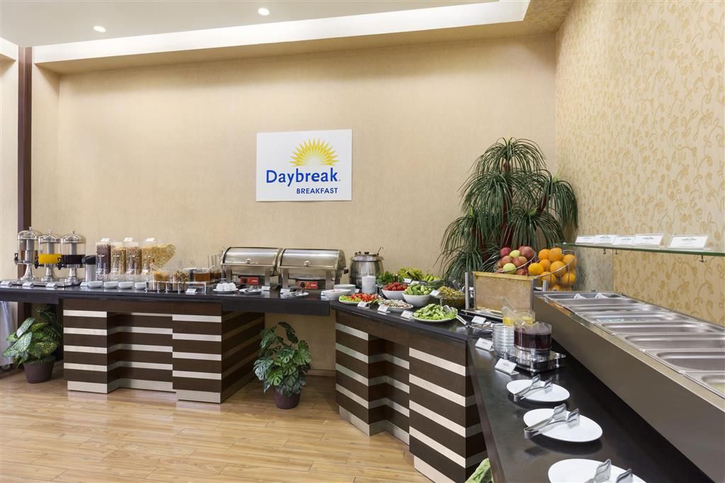 Zona para desayuno tipo bufé con un letrero que dice 'Daybreak Breakfast', que ofrece una variedad de opciones de comida y una barra de bufé.