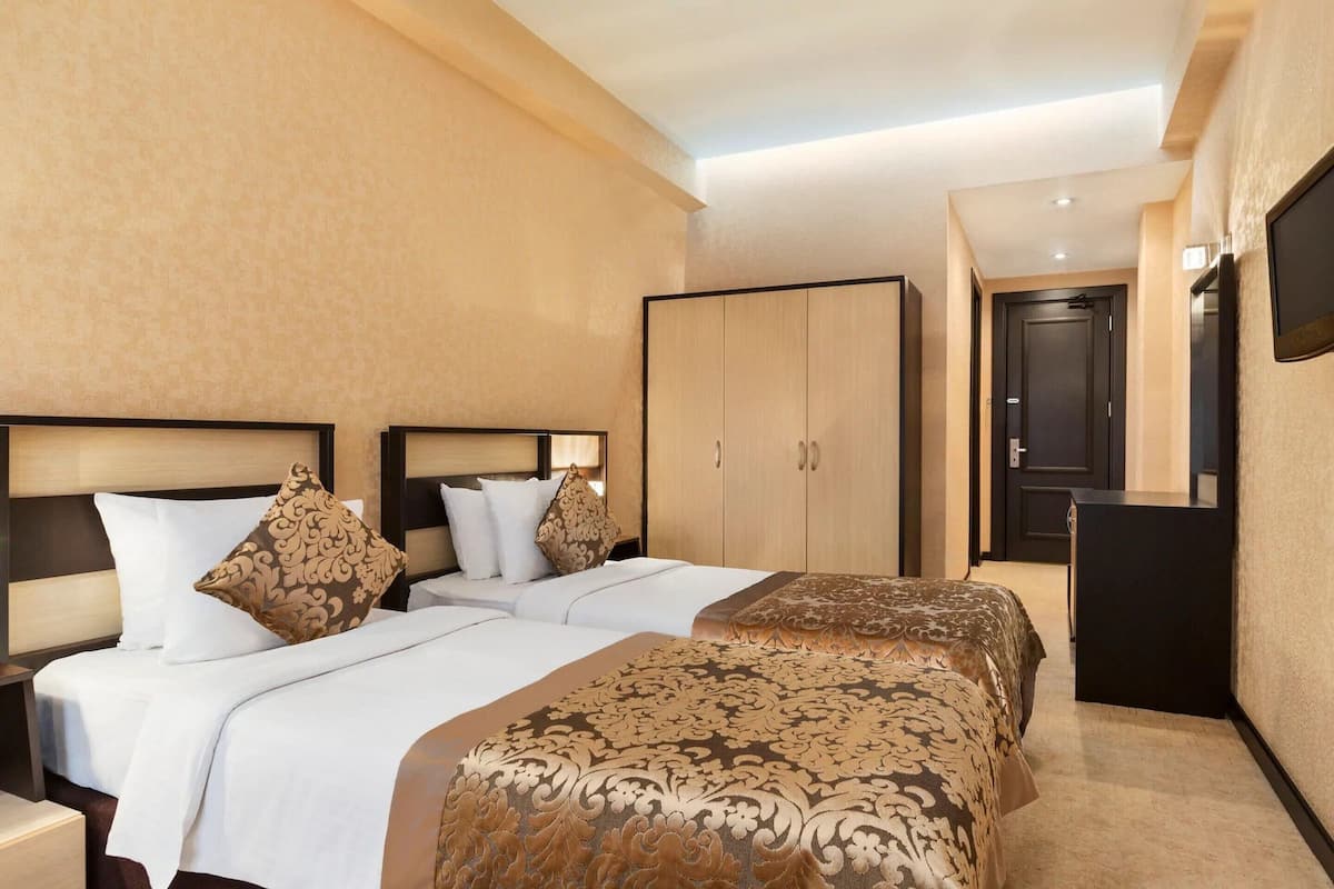 Ein Hotelzimmer mit zwei Betten, einem Kleiderschrank, einem Schreibtisch und einem Fernseher.