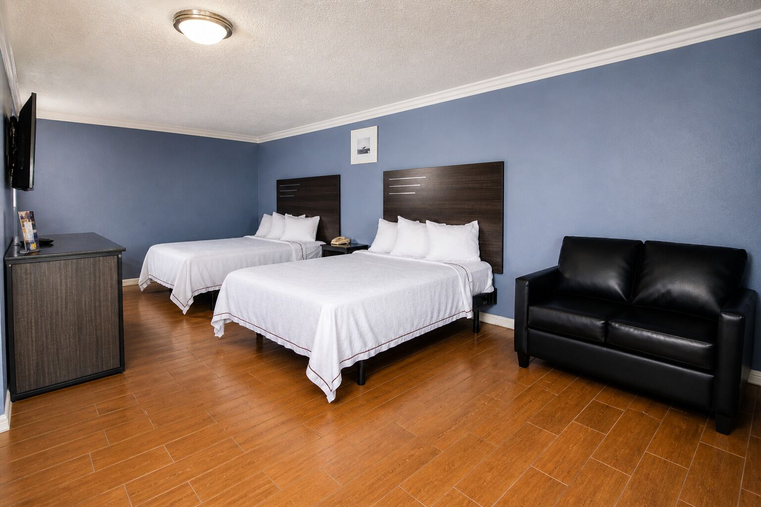A hotel room with two beds, a black leather chair, a desk, and a flat-screen TV.