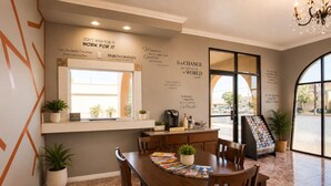 A modern dining area with a wooden table, chairs, a coffee machine, and a window with a view. - Big A Motel & Suites Near Disneyland Orange County (Orange)