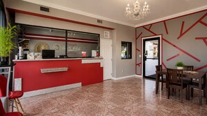 A hotel lobby with a red reception desk, a chandelier, a dining area with wooden chairs, and a patterned floor. - Big A Motel & Suites Near Disneyland Orange County (Orange)