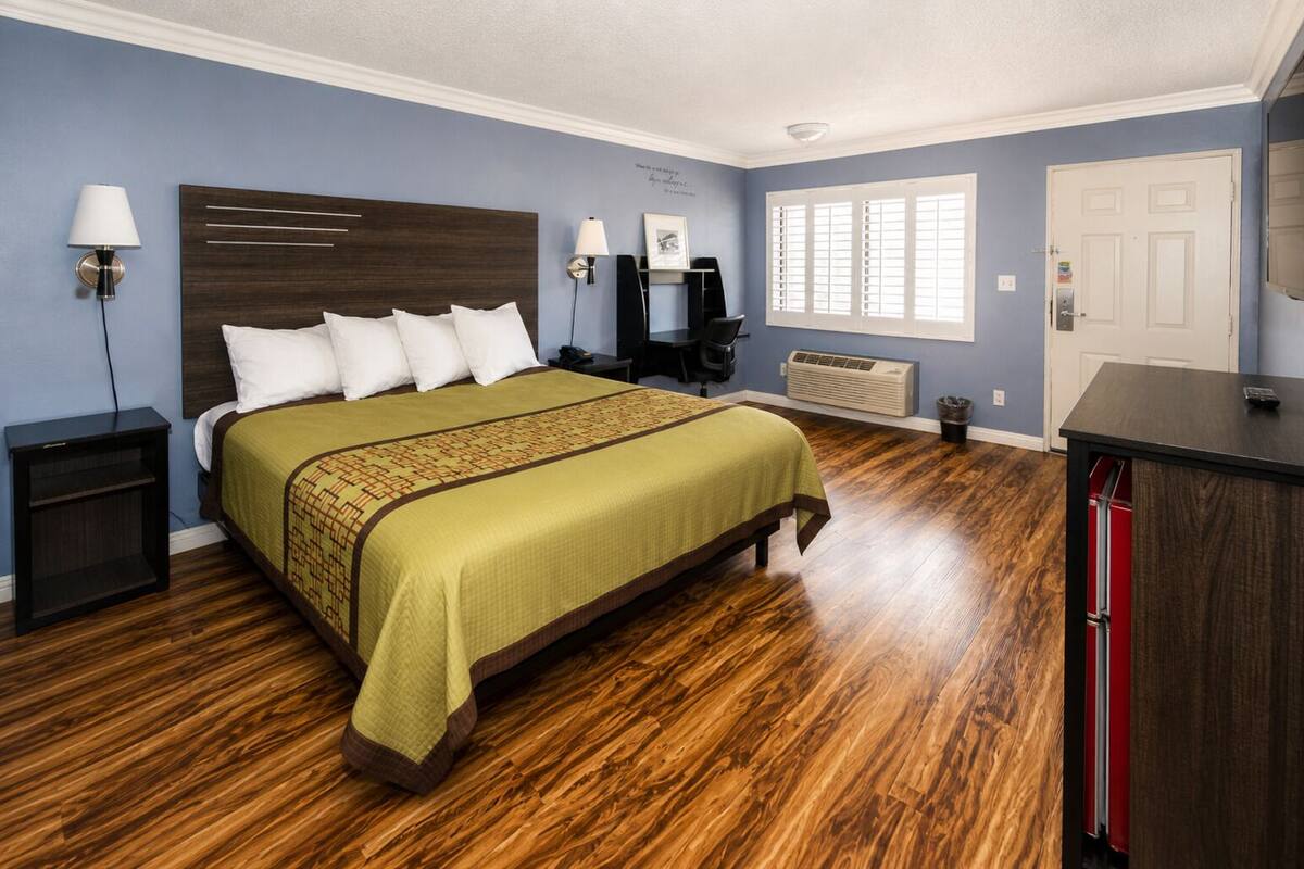 Una habitación de hotel con una cama grande, un escritorio, una silla, una lámpara, un calentador y una puerta.