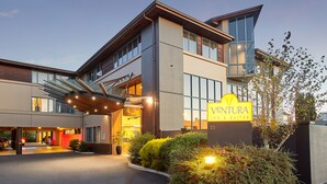 Un hotel moderno con una entrada destacada, un letrero que dice 'Ventura Inn & Suites' y un área exterior bien iluminada con jardines.