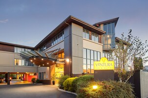 Un hotel moderno con una entrada destacada, un letrero que dice 'Ventura Inn & Suites' y un área exterior bien iluminada con jardines.