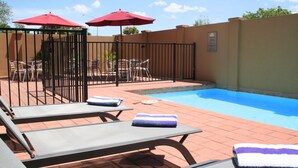 Zona de piscina con sillones de descanso y sombrillas rojas.