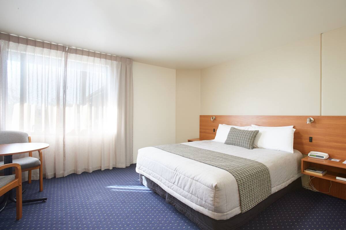A hotel room with a bed, a chair, a small table, and a nightstand.