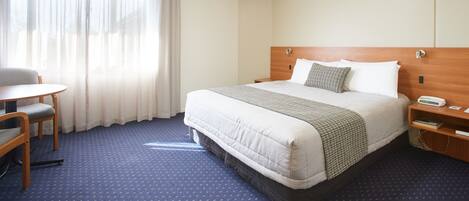 Une chambre d’hôtel avec un lit, une chaise, une petite table et une table de chevet.