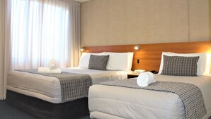 Una habitación de hotel con dos camas, cabeceros de madera y un ventanal con cortinas.