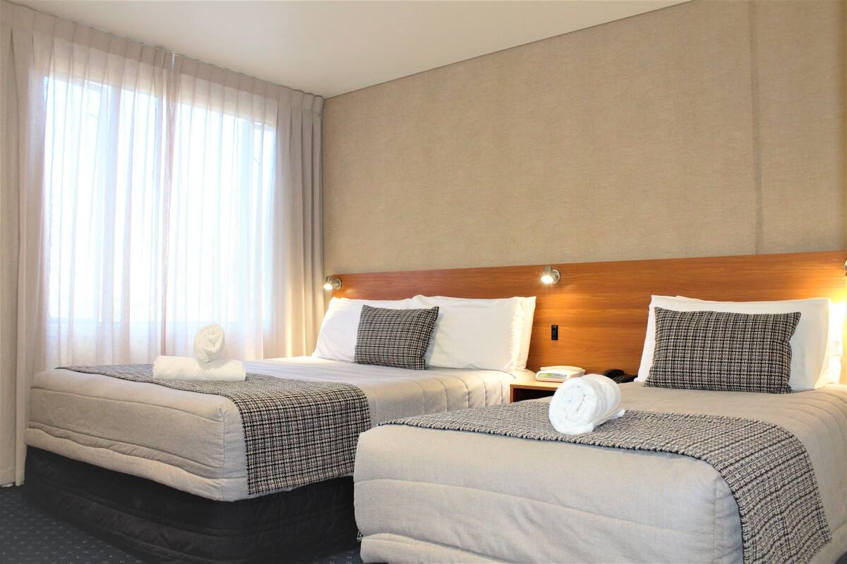A hotel room with two beds, a wooden headboard, and a large window with curtains.