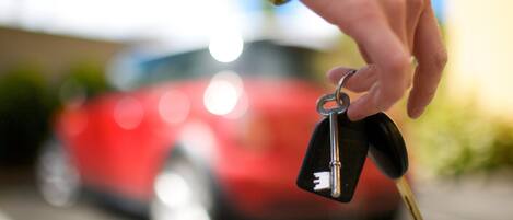 A hand holding car keys with a blurred red car in the background.