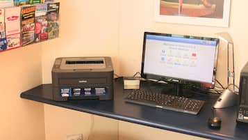 Una mesa de recepción de hotel con una computadora, una impresora y varios folletos de viaje.