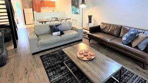 A modern living room with a grey sofa, a brown leather sofa, a wooden coffee table, and a black and white rug.