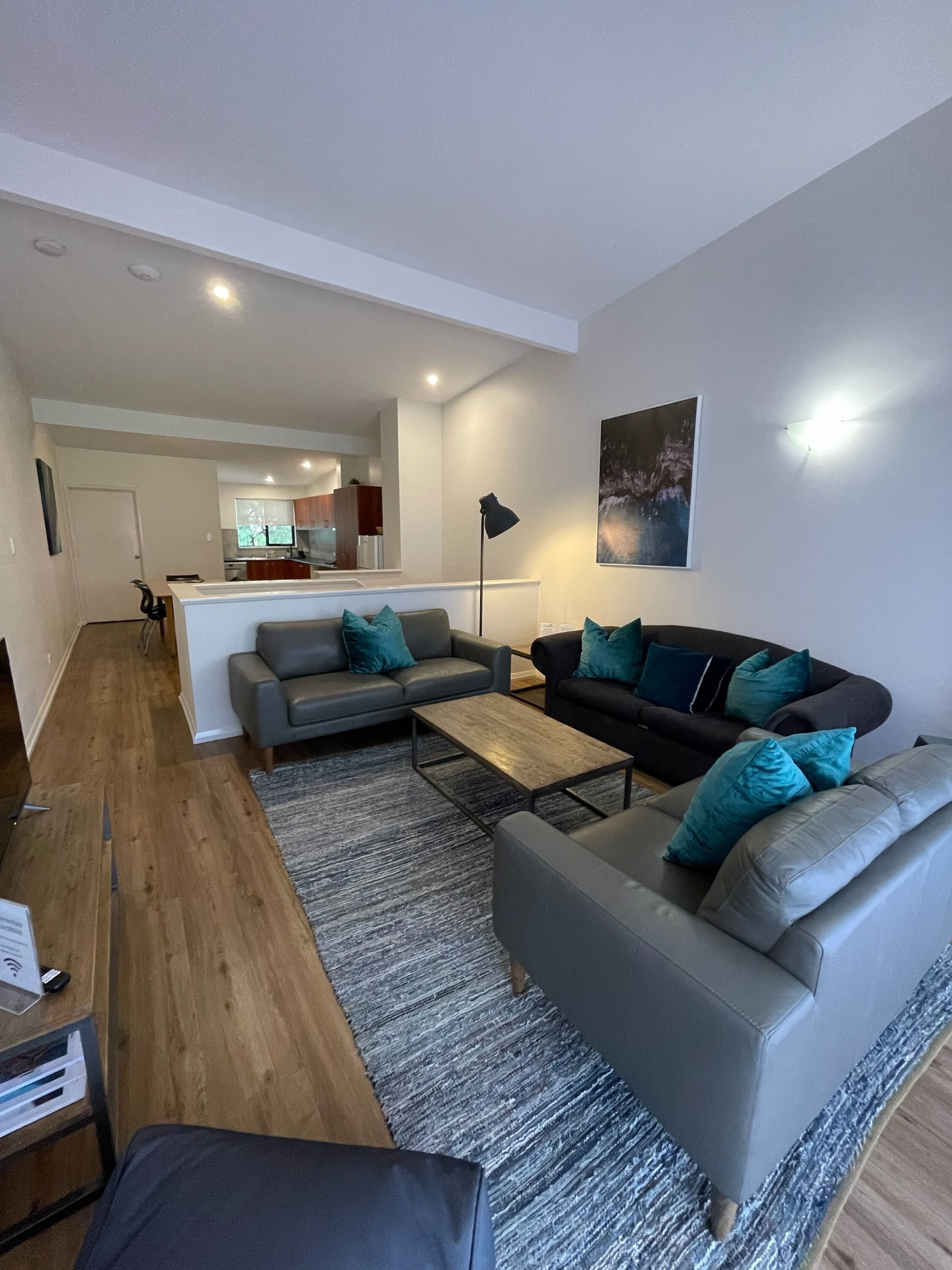 A modern living room with a grey sofa, a black sofa, and a coffee table. There is a kitchen in the background with a fridge and a microwave.