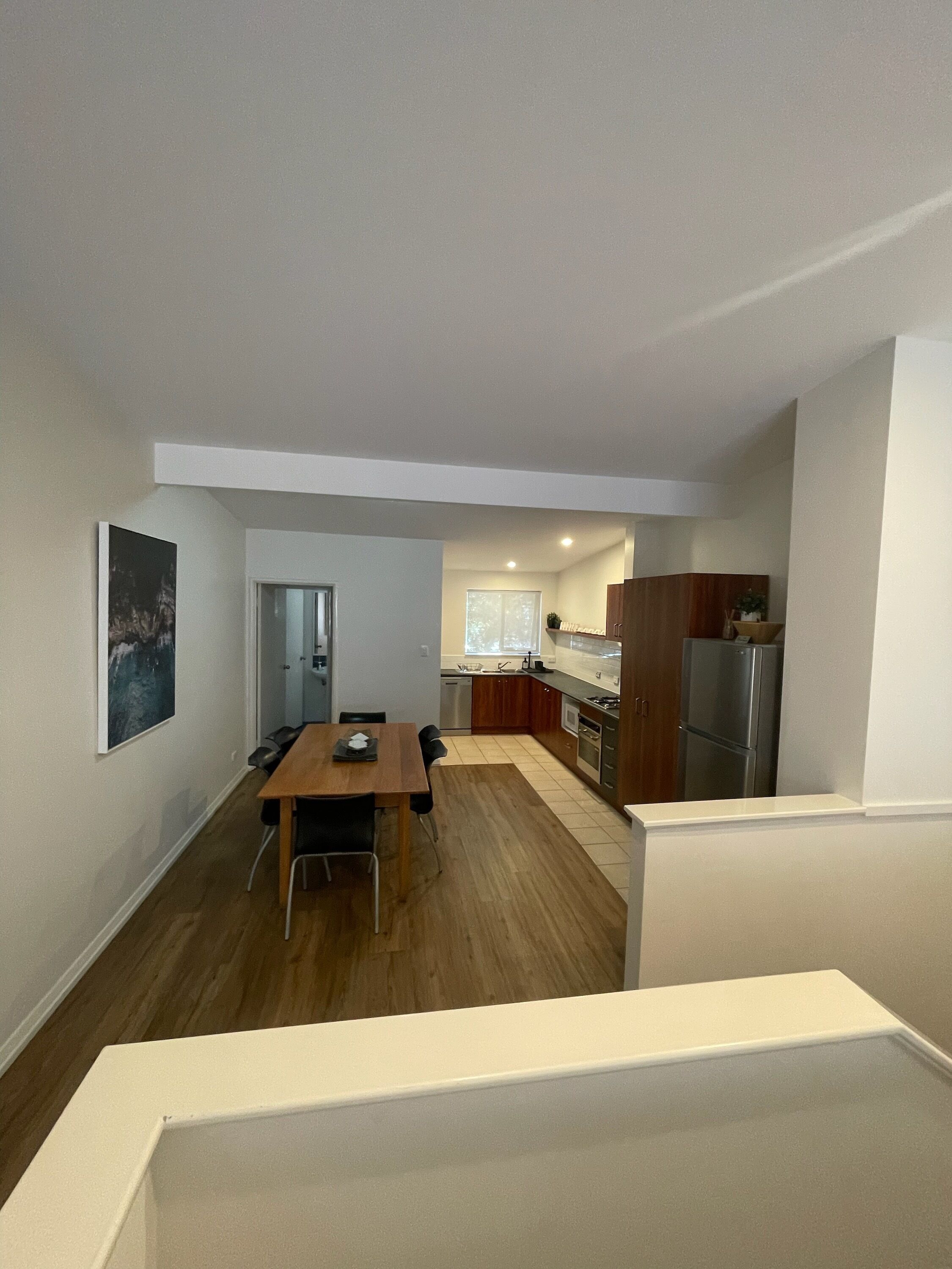 A modern kitchen with wooden cabinets, a stainless steel refrigerator, and a dining area with a wooden table and chairs.