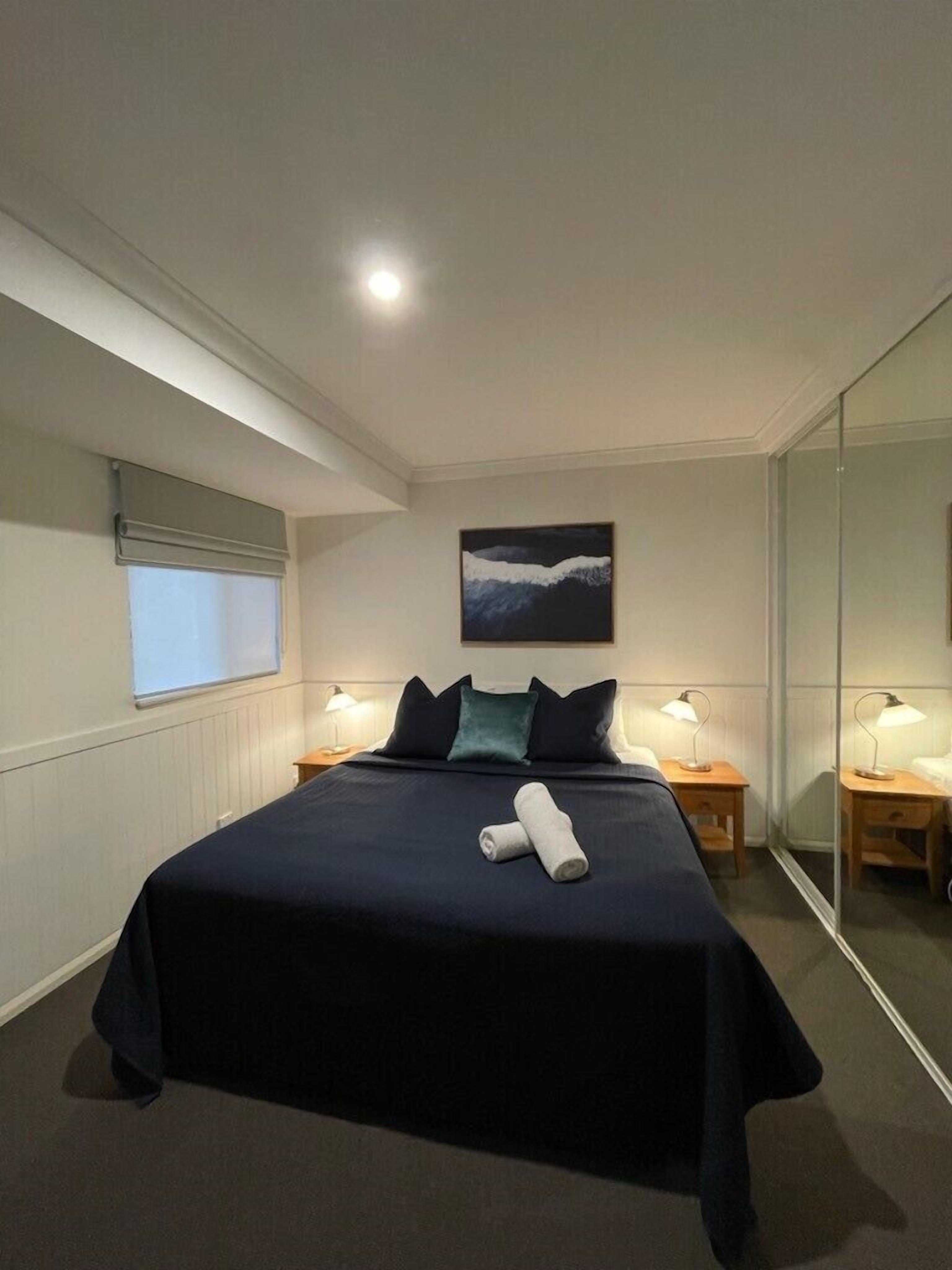 Una habitación de hotel moderna con una cama grande, un cuadro en la pared y un espejo que refleja la estancia.