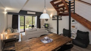 A modern living space with a wooden dining table, a sofa, a TV, and a staircase.