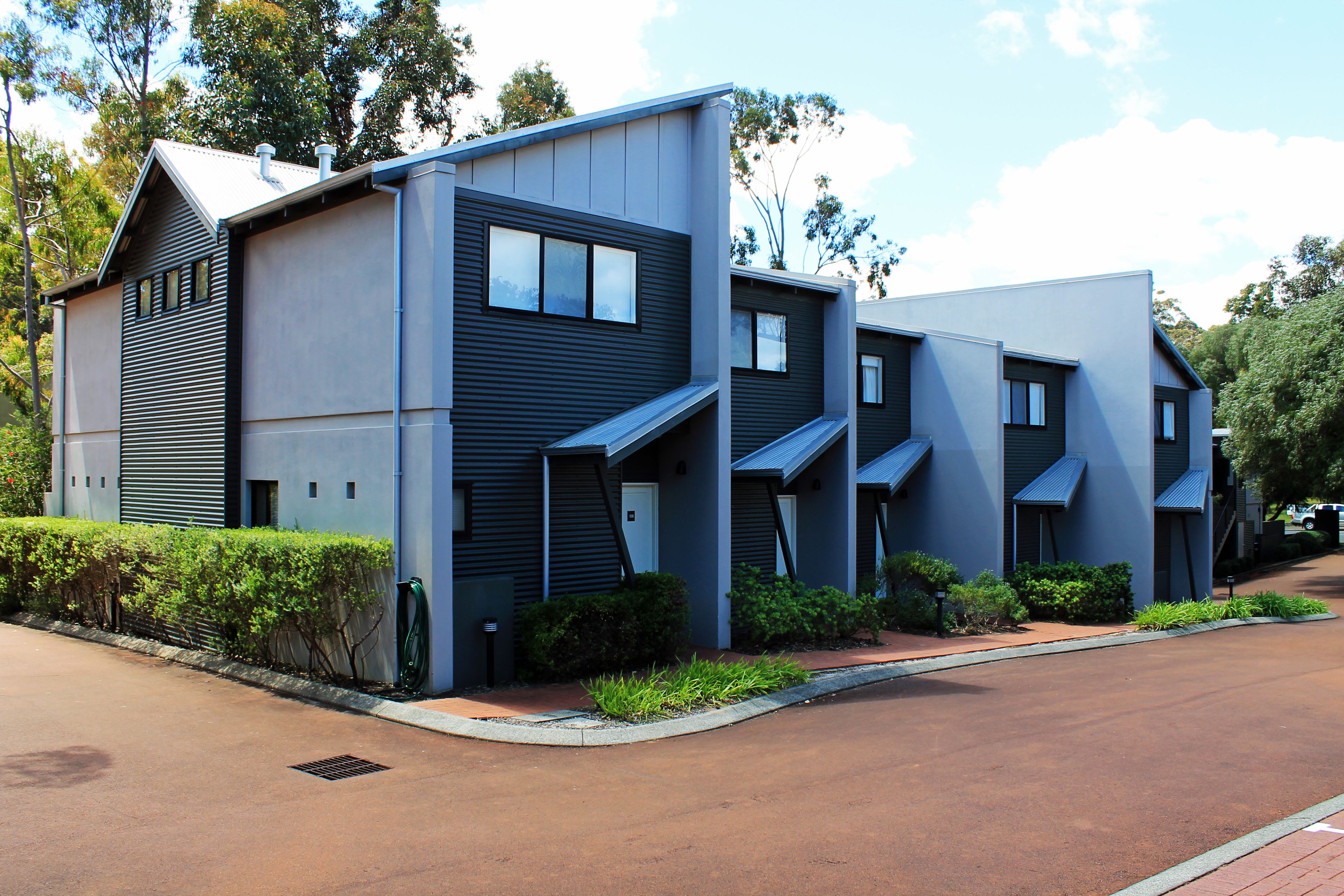 A modern two-story residential building with a flat roof, large windows, and a well-maintained garden.