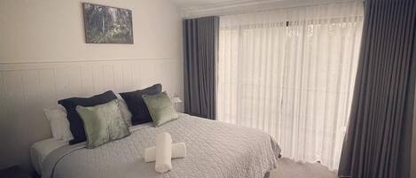 Una cama bien tendida con colcha, almohadas y una toalla enrollada. Se ve un ventilador de techo arriba.