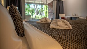 A hotel room with a bed, a patterned pillow, a neatly folded towel, and a view of greenery through a large window. - Forest Lodge Resort (Pemberton)