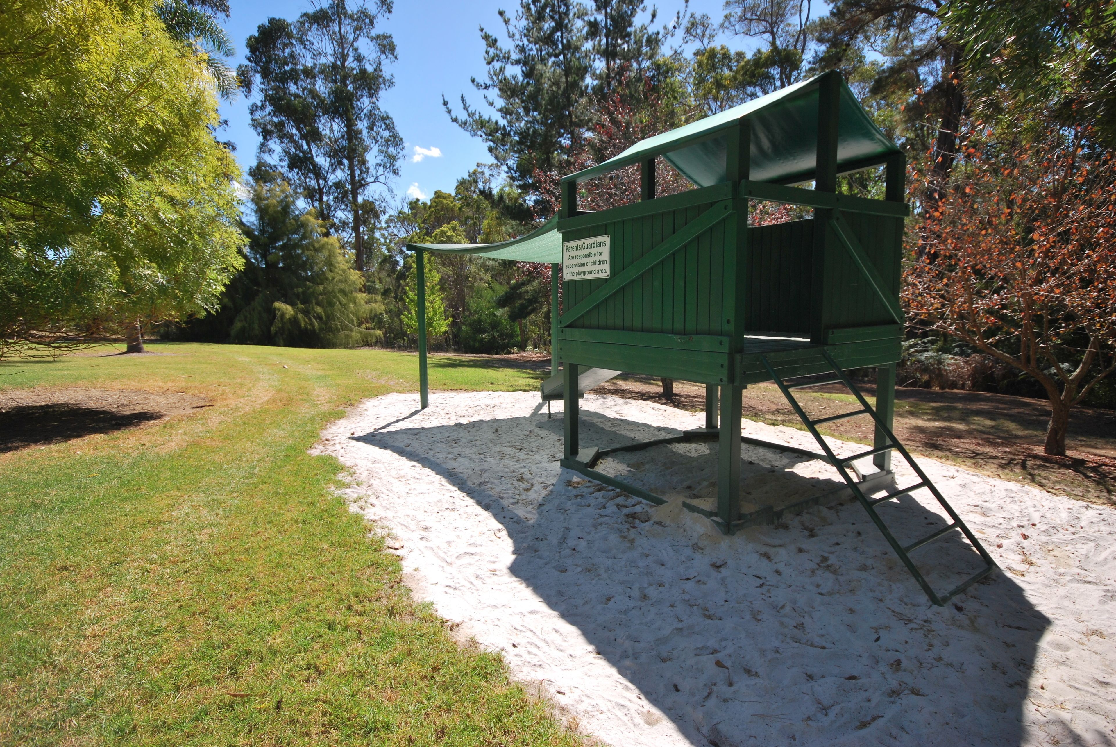 A green play structure with a sign, surrounded by trees and grass.