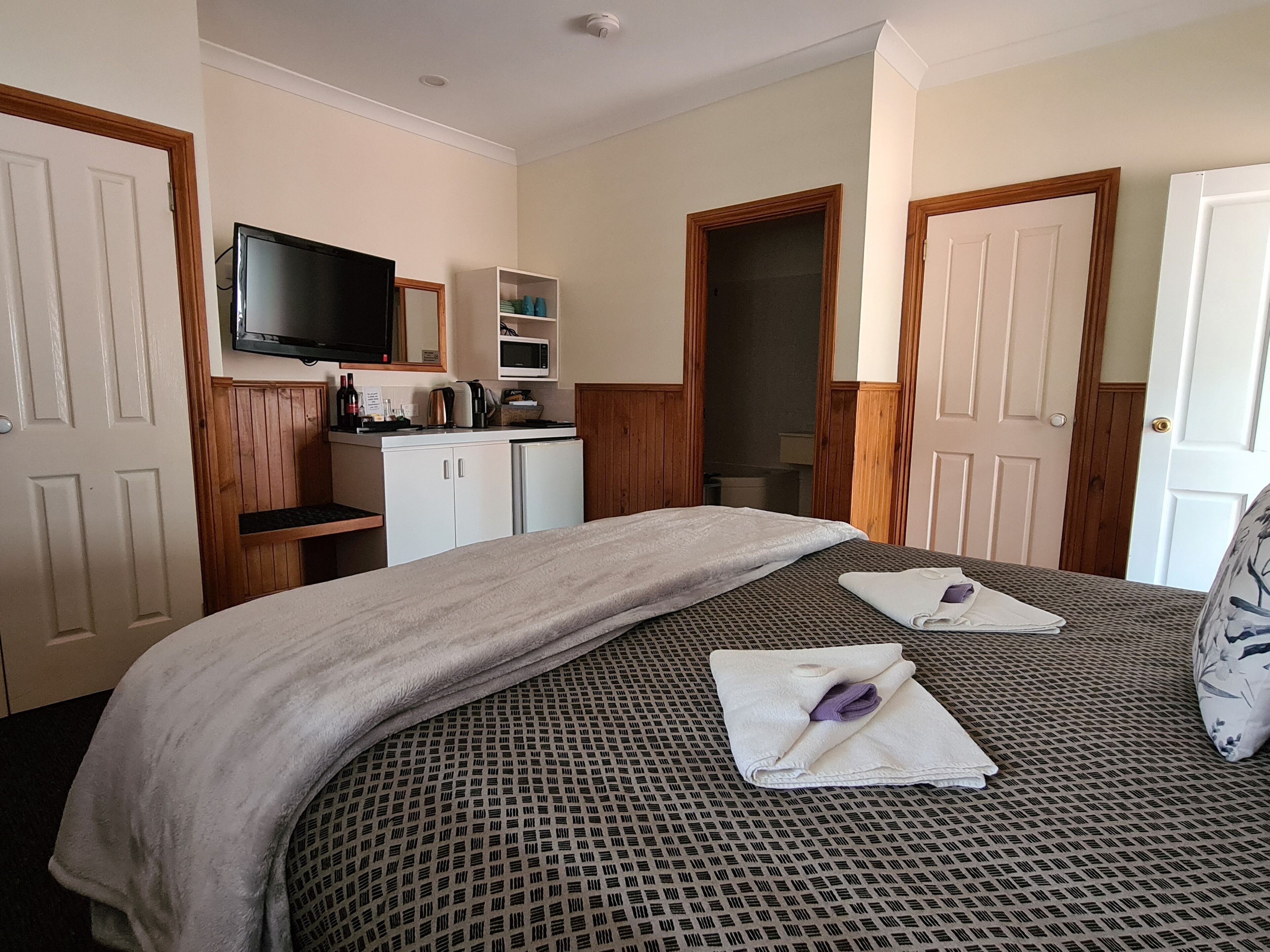 A hotel room with a bed, a television, a kitchenette, and a bathroom.