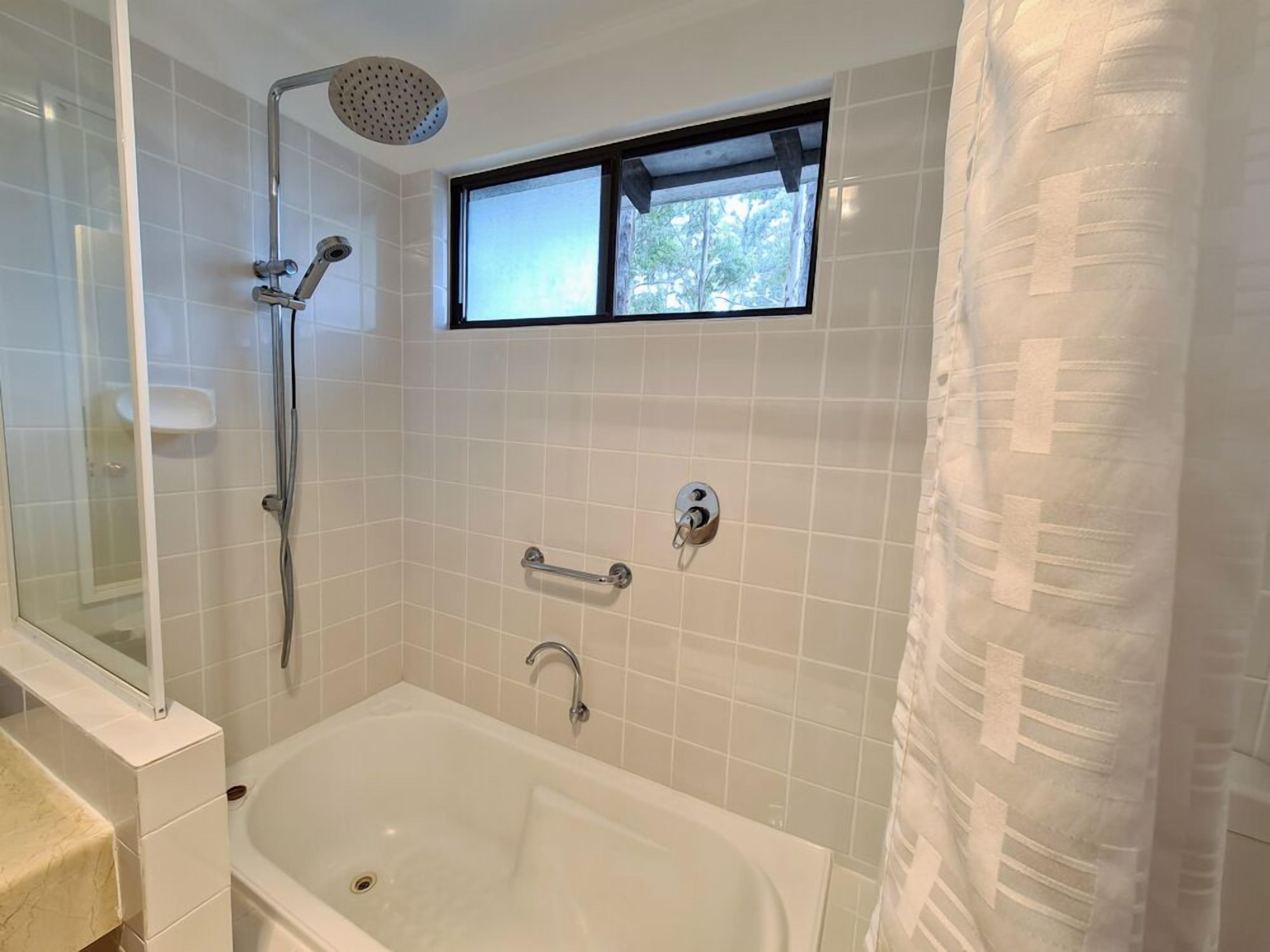 A modern bathroom with a bathtub, a shower, and a window.