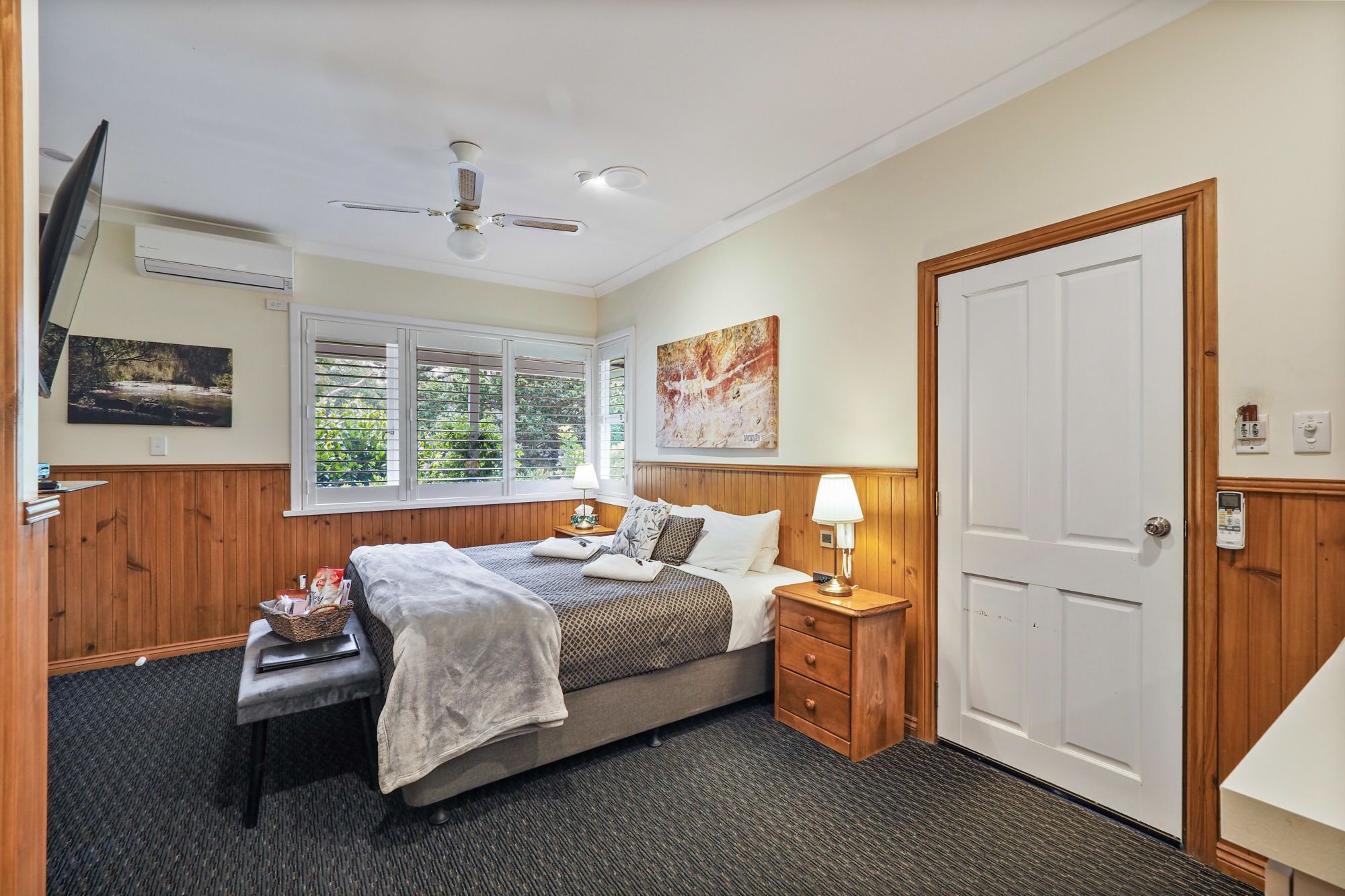 A bedroom with a bed, bedside tables, a ceiling fan, a window with blinds, and a door.