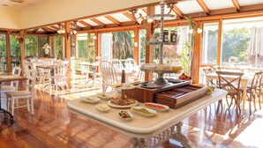 A spacious dining area with wooden beams, large windows, and a variety of food items on a central serving table. - Forest Lodge Resort (Pemberton)