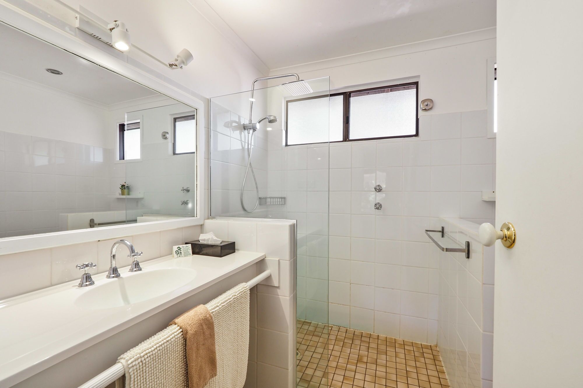 A modern bathroom with a large mirror, two sinks, a shower, and a toilet.