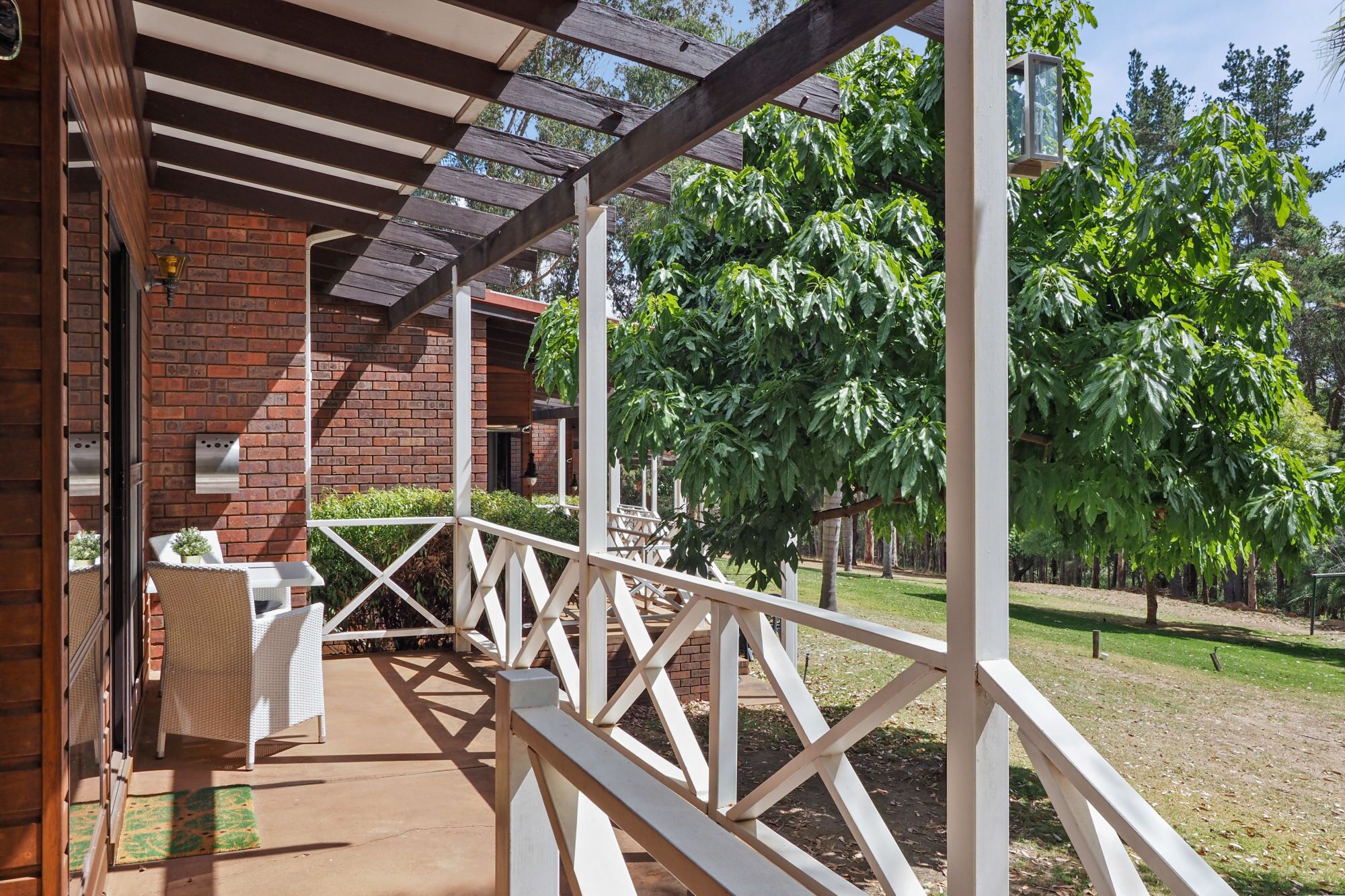 A covered outdoor area with a brick wall, white railing, and a table with chairs.