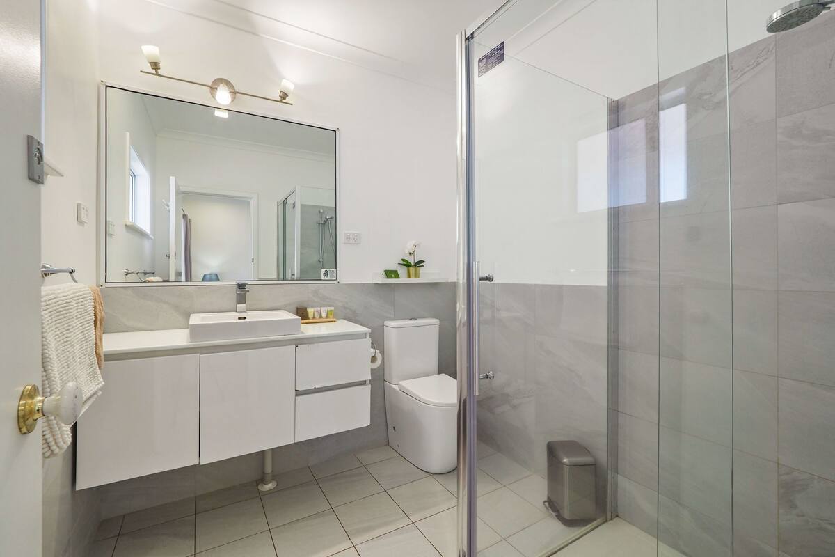 A modern bathroom with a glass-enclosed shower, a white sink, and a toilet.