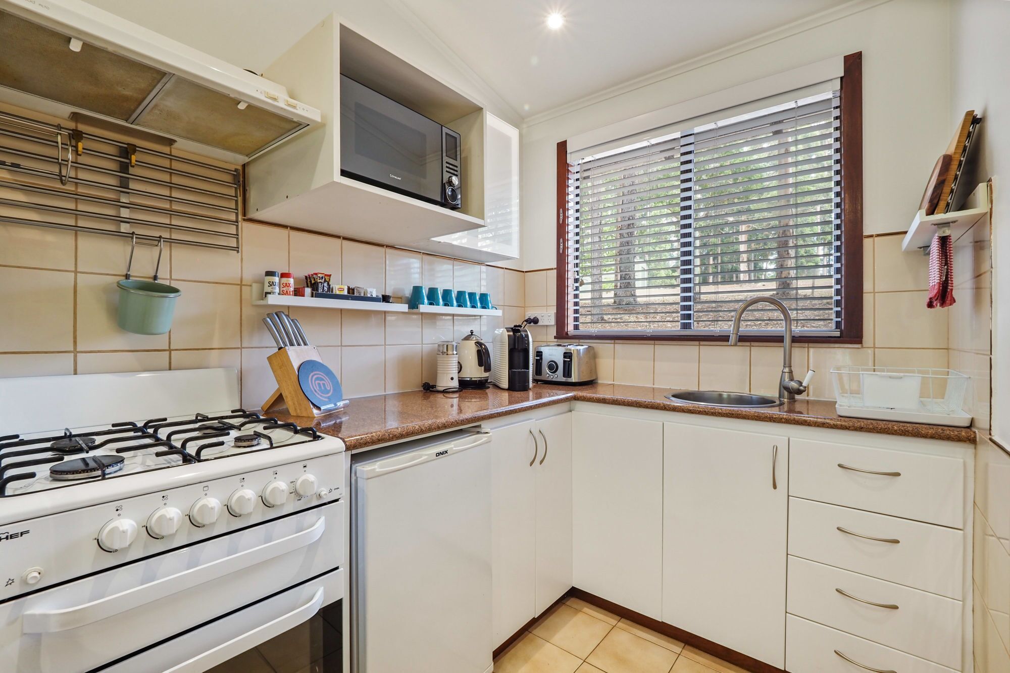 A kitchen with a gas stove, oven, microwave, and a window with blinds.