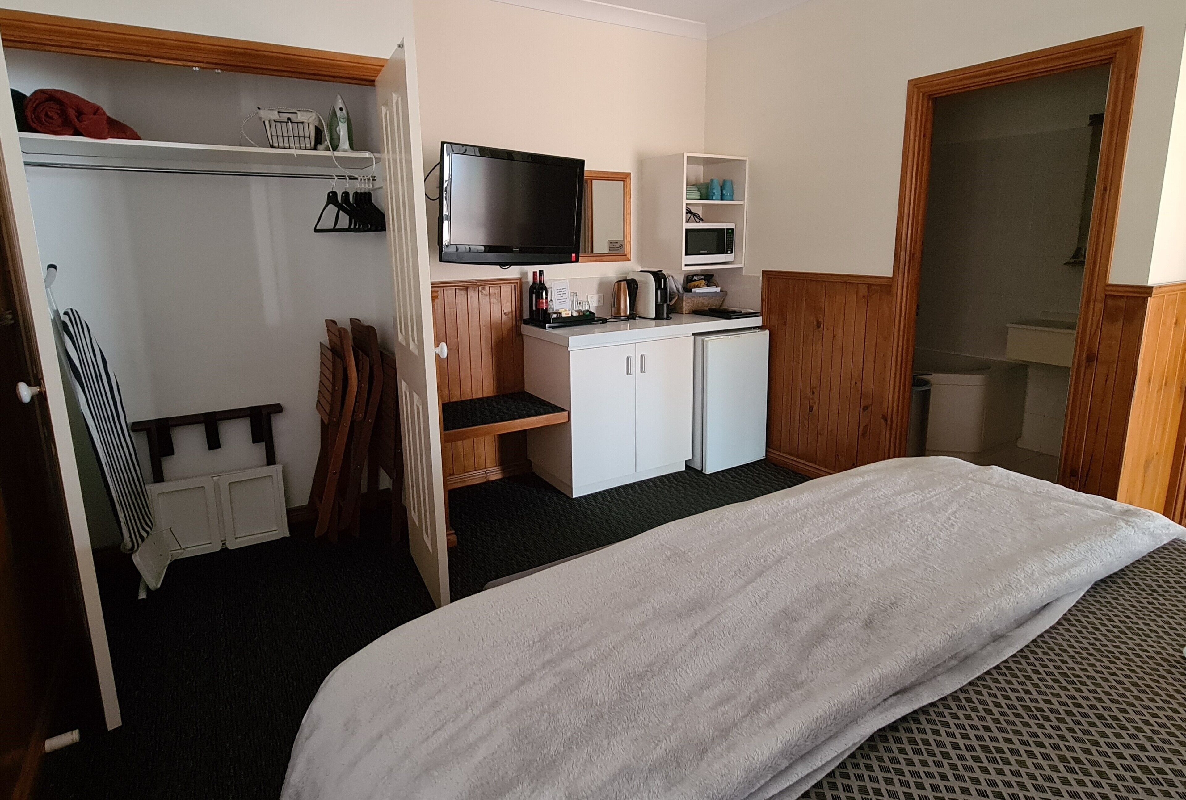 A compact hotel room with a bed, a kitchenette, a TV, and a shower area.