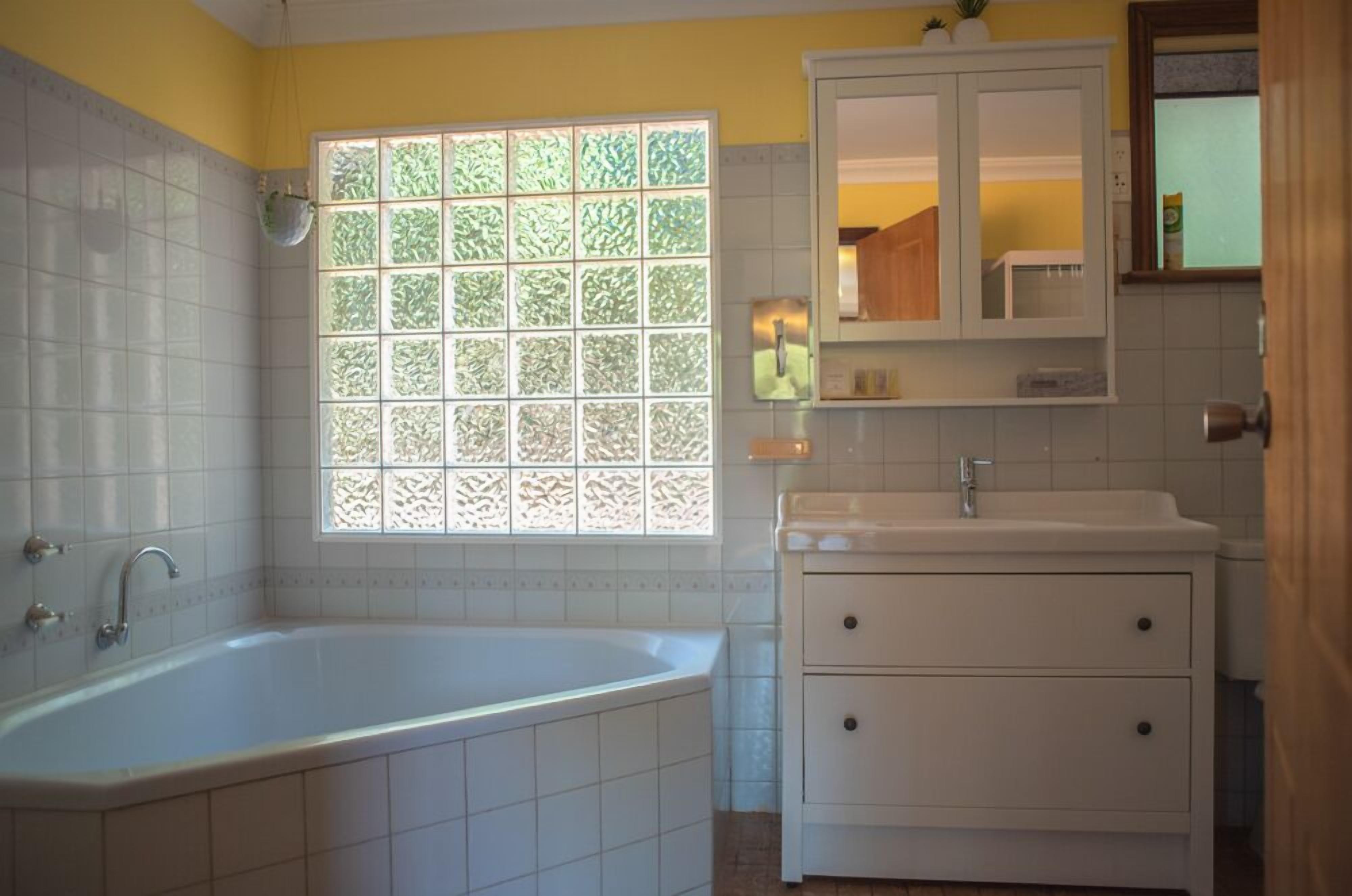 Une salle de bain avec une baignoire, une fenêtre ornée de vitraux, un lavabo et un meuble de rangement.