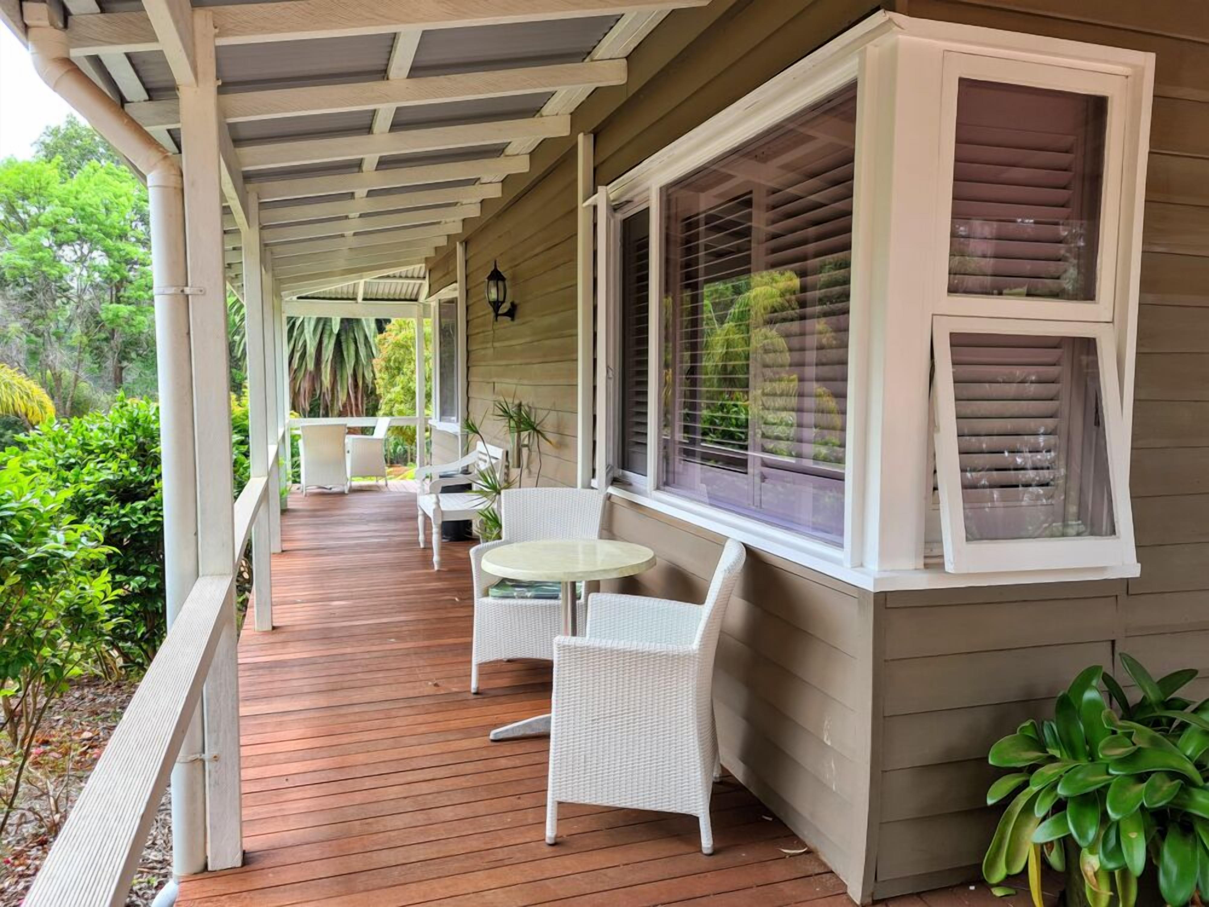 A covered porch with white wicker furniture, a small table, and a window with blinds.