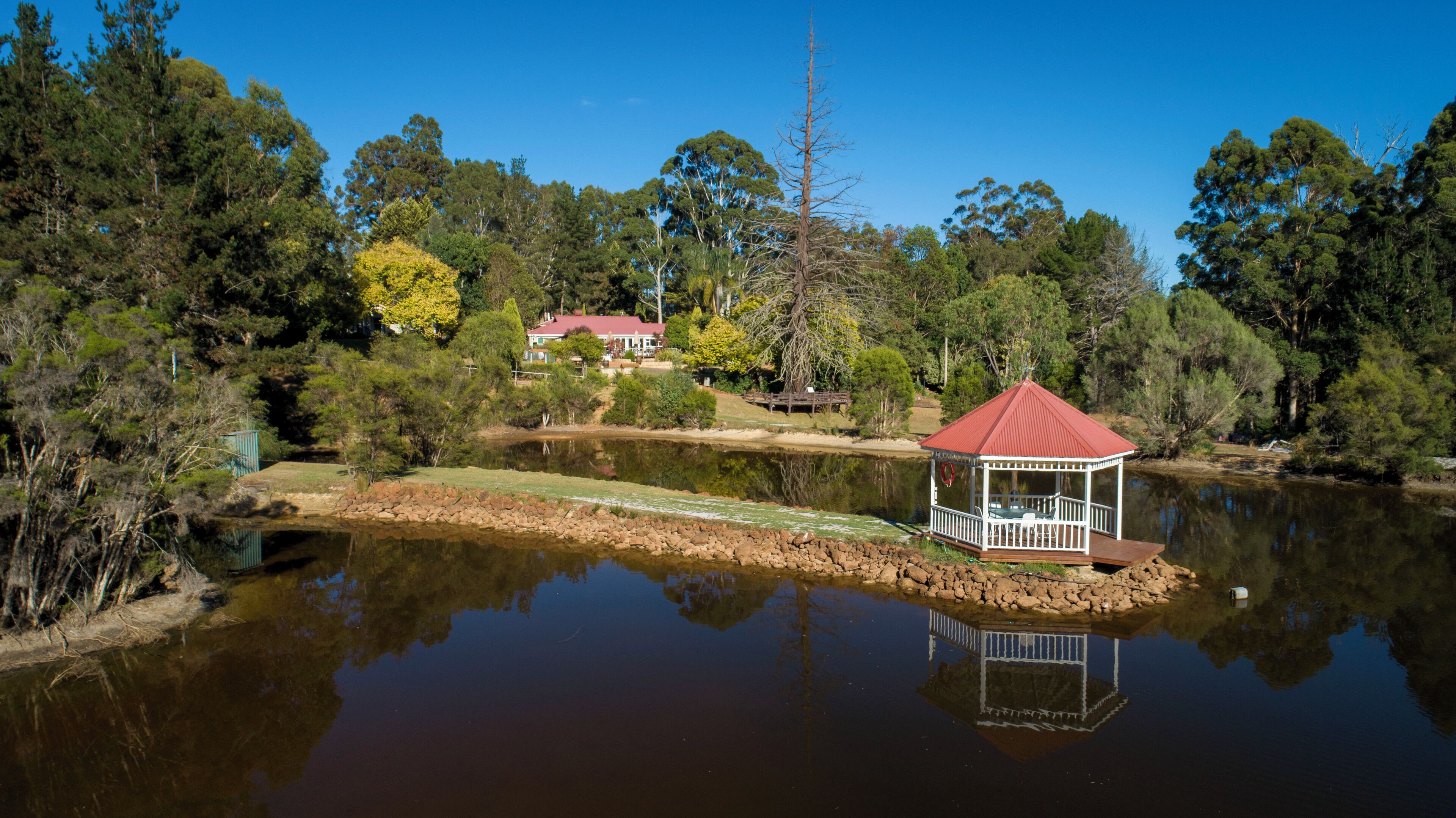 Ein Pavillon am See, mit einem Haus im Hintergrund.