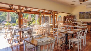 A spacious restaurant with wooden tables and white chairs, large windows, and a view of greenery. - Forest Lodge Resort (Pemberton)