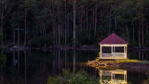 A gazebo on a lakeside island with a red roof and white railing, surrounded by dense forest. - Forest Lodge Resort (Pemberton)