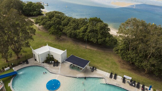 En stor udendørs swimmingpool med udsigt til havet og en bysilhouet i baggrunden.