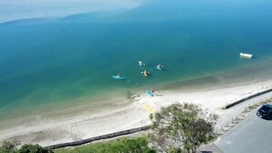 Kystområde med kajakker på vandet og en strand med vej og bil.