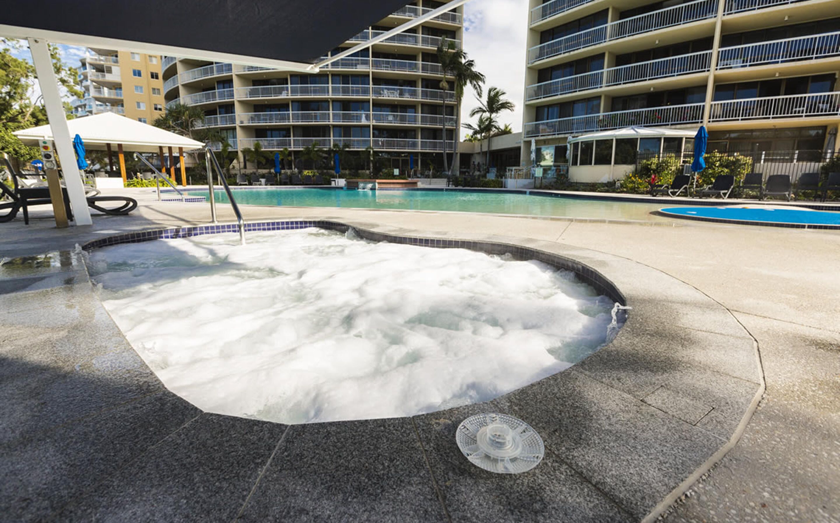 Un bain à remous entouré d’une piscine, avec un immeuble à plusieurs étages en arrière-plan.