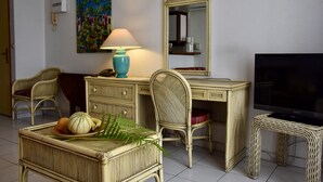 A room with a desk, two wicker chairs, a television, a lamp, and a painting on the wall.