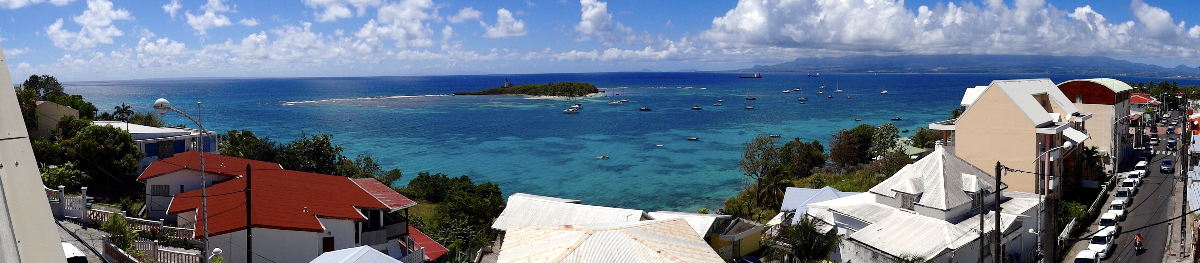 Une vue sur la côte, avec une eau d’un bleu limpide, des bateaux et des bâtiments aux toits rouges.