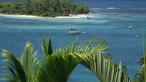 A tropical beach with clear turquoise waters, a small island with palm trees, and a boat anchored near the shore.
