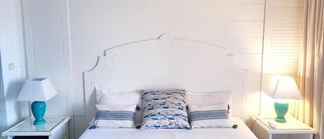 Een keurig opgemaakt slaapkamer met een wit bed, bijpassende nachtkastjes en een decoratief plafond.