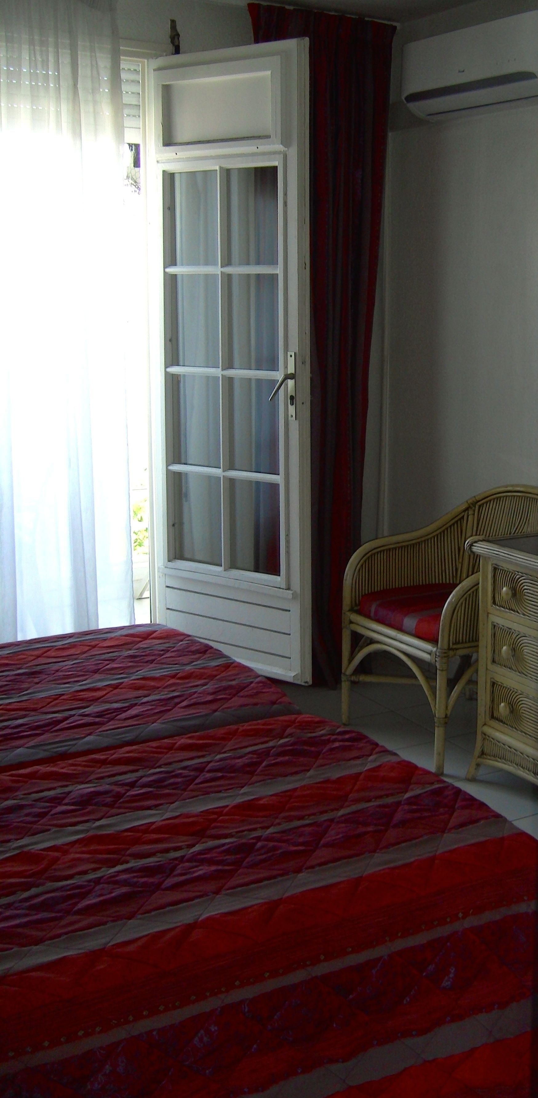 Ein Schlafzimmer mit einem Bett, einem Korbsessel, einem Kleiderschrank und einer Klimaanlage.