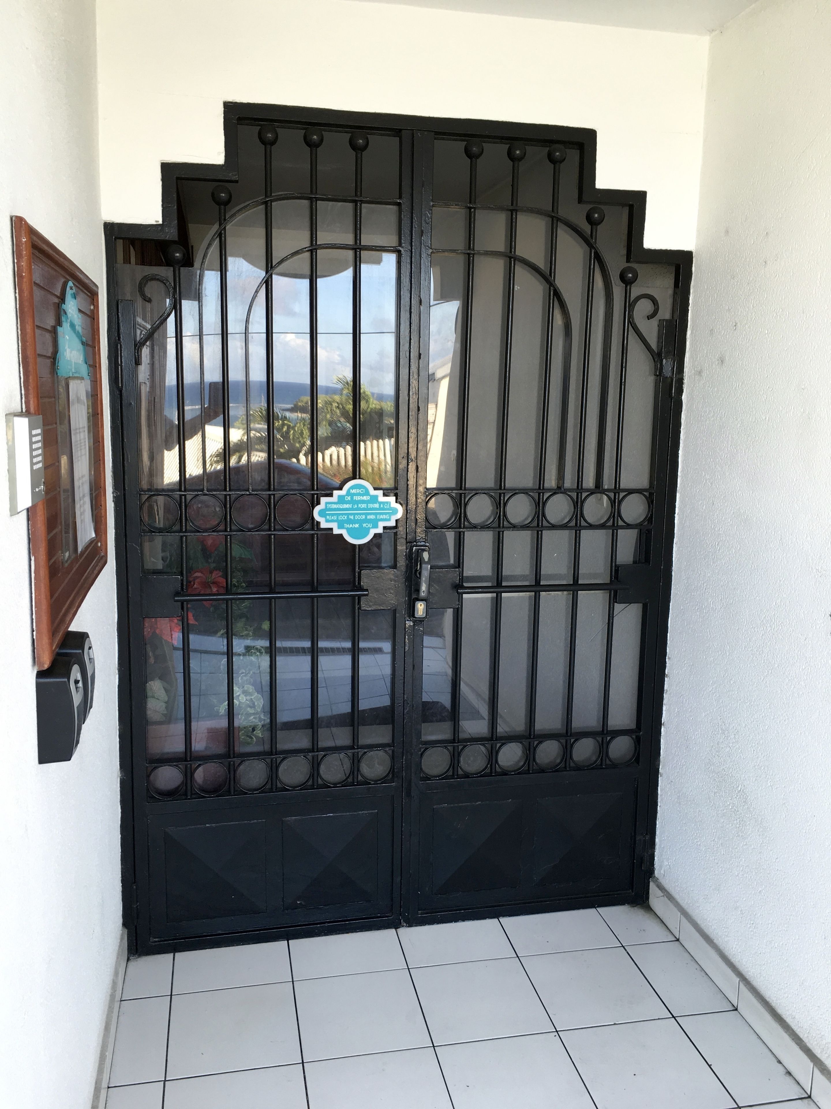 Una reja de metal negro con un diseño decorativo, un letrero pequeño y vistas al exterior.