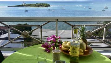 Enjoy the ocean view from this balcony with a table set for two, featuring a vase of flowers and a refreshing drink.