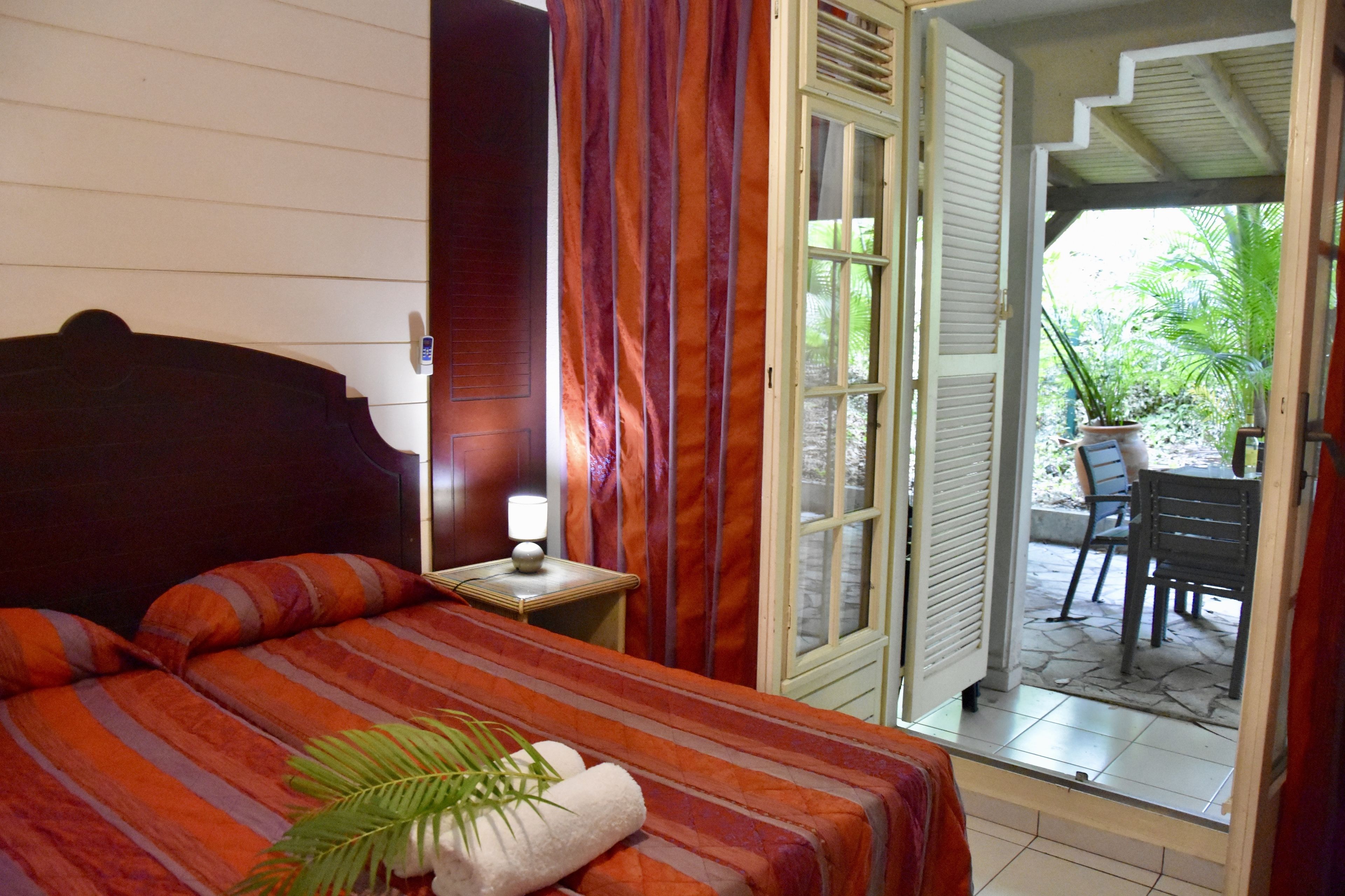 A bedroom with a bed, a nightstand, a lamp, and a view of an outdoor patio area.